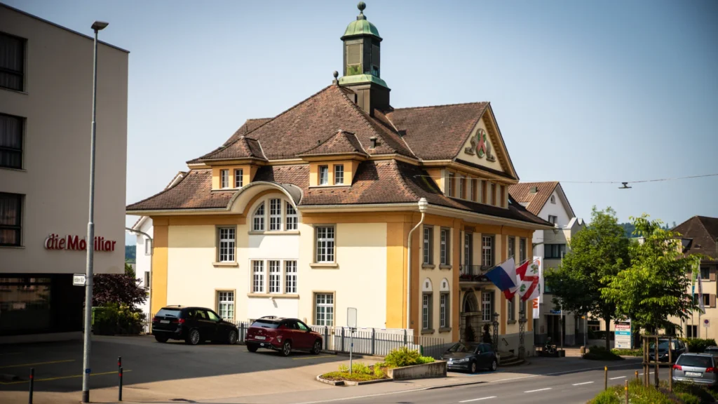 Gebäude der Gemeindeverwaltung Hochdorf im Kanton Luzern mit markantem Dach und Turm, umgeben von Strassen und parkenden Autos.